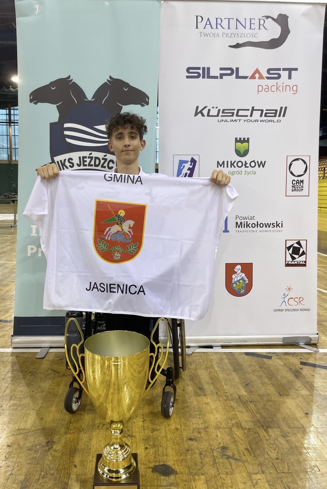 Adam Kamela trzymający materiał na którym jest herb gminy.
